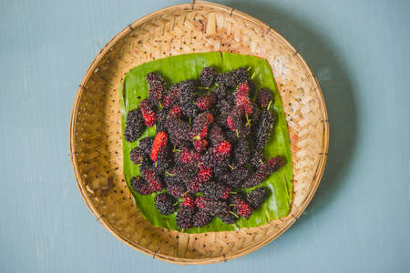 A large number of ripe mulberries, followed by banana leaves, are in wicker baskets.の写真素材