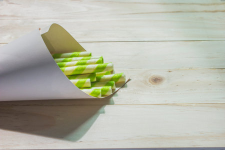 Green and white striped wafers are wrapped in paper and placed on a woodenの写真素材