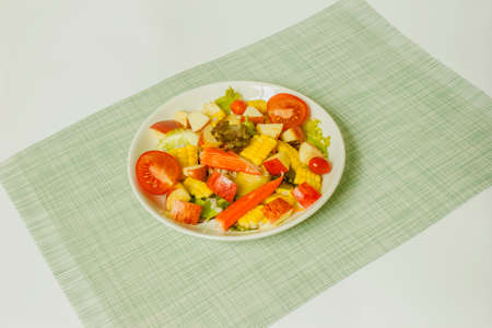 Mixed vegetable and fruit salad with crab sticks on a white plate, ready to serveの写真素材