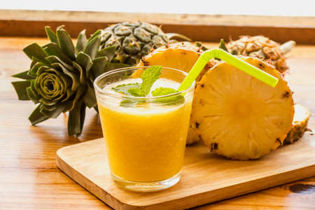 Pineapple blended on top of mint leaves and pineapple sliced on a wooden cutting board.の写真素材
