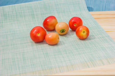 Six red tomatoes are placed on a cloth and board.の写真素材
