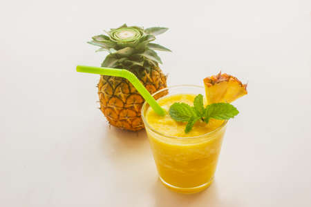 Sweet and refreshing pineapple smoothie decorated with mint leaves and straws on white background.の写真素材