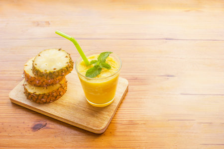 Pineapple blended on top of mint leaves and pineapple sliced on a wooden cutting board.の写真素材