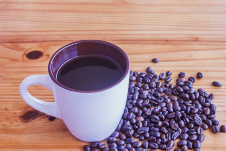 A cup of black coffee and coffee beans piled on an old wooden floor.の写真素材