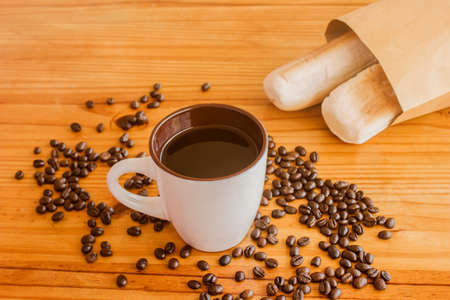 A cup of black coffee and coffee beans are piled on the floor with a bag of bread.の写真素材
