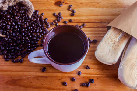 A cup of black coffee and coffee beans are piled on the floor with a bag of bread.の写真素材