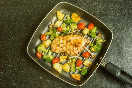 Grilled chicken breast steak with potatoes, cherry tomatoes, broccoli and sauce in pan ready to serve, top view.の写真素材