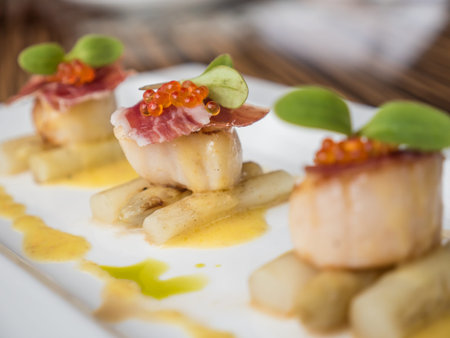 Seared scallops with salmon roe, ham and asparagus on plate