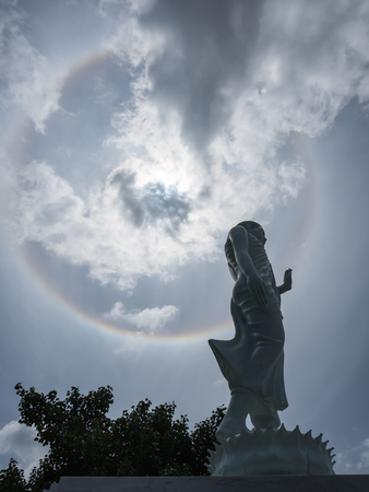 Buddha statue and sun halo on blue sky backgroundの写真素材