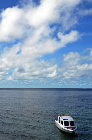 A boat is waiting in a calm ocean, under a blue sky.の写真素材