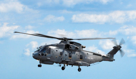Merlin Military Helicopter flying right to left against a blue sky.