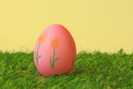red Easter egg with floral motif on green artificial grass before yellow backgroundの写真素材