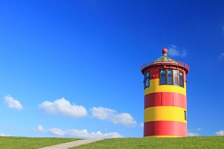 Lighthouse Pilsum on the dike in East Frisia, North Sea, Lower Saxony, Germany, against a blue skyの写真素材
