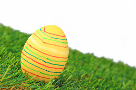 Colorful dyed Easter egg on synthetic grass in front of a white background