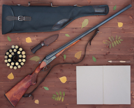 The gun, bandolier, knife, leather case for rifle and a notebook with a pencil. Wooden background. Flat lay concept. Top view.の写真素材