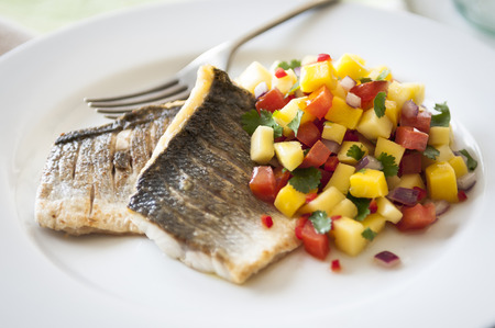 Seabass fillets withwatermelon, pineapple and mango salsa on a white plate on wooden backgroundの写真素材