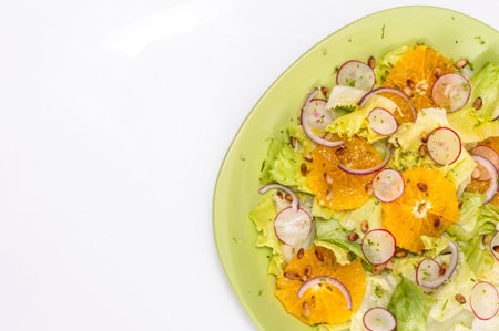 Orange and radish salad with red onion and pine nuts on a green plate, isolated on whiteの写真素材