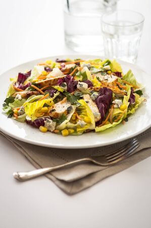 Chicken and sweetcorn salad place setting with fork and napkin to the foreground and glasses behindの写真素材