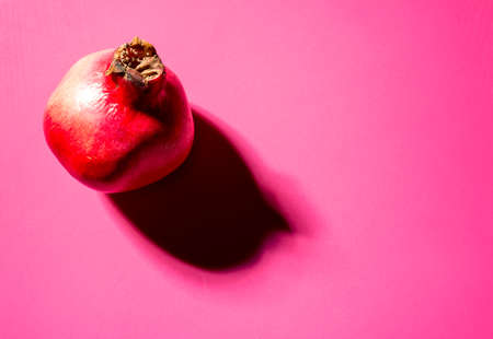 A single pomegranate on a pink background with a strong shadowの写真素材