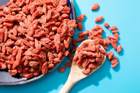 Goji berries on a wooden spoon and blue plate on a blue backgroundの写真素材