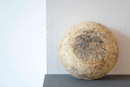 A Berkswell Cheese round on slate leaning against a white wall