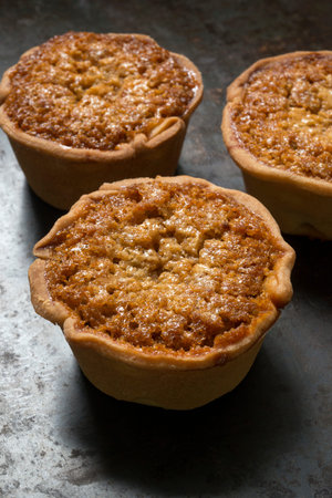 Three individual treacle tarts on a baking tray