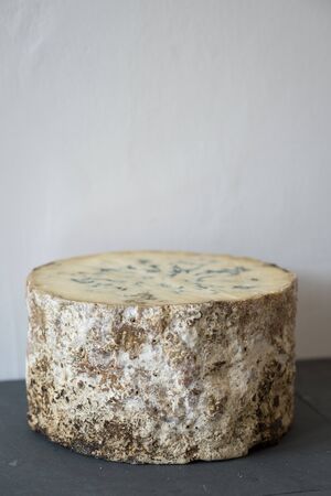 A whole Stitchelton cheese round on slate against a white wallの写真素材