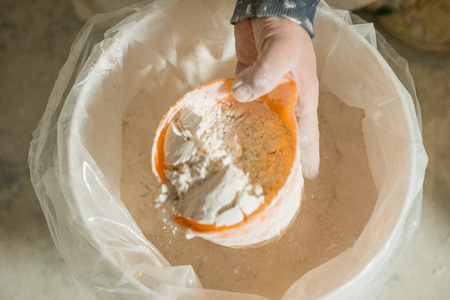 A hand with plaster orange dipper scooping up powder plaster from a large plastic bucketの写真素材