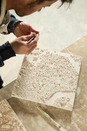 Man working on a fine component of a 3D city map model made of plaster.