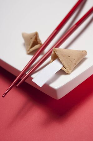 Cracked fortune cookie with blank piece of paper and a pair of red chopsticks on edge of a white board.の写真素材