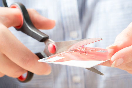 Close up shot of the hands of a person in Blue Shirt using plastic scissors to destroy a debit or...
