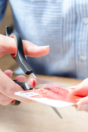 The hands of a person in Blue Shirt holds plastic scissors, ready to cut a bank card in two at a wooden deskの写真素材