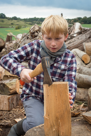 Young woodcutter boy chopping a piece of wood with an axeの写真素材