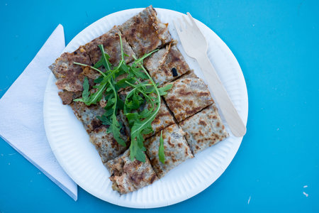 Overhead shot of a crepe in bite-size pieces served in a paper plate with a plastic fork and topped with greensの写真素材