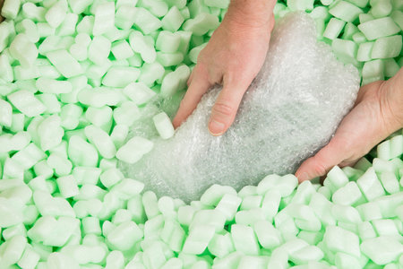 Hands placing a bubble wrapped parcel in polystyrene loosefill.