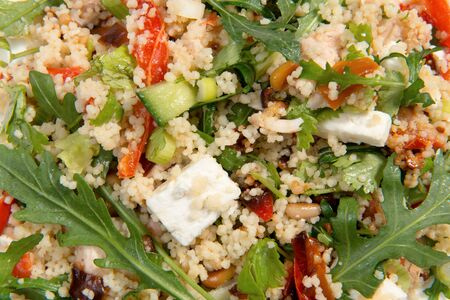 Overhead close shot of a couscous salad on a white plate. The salad ingredients consist of rocket, feta cheese, pinenuts, cucumber and roasted peppersの写真素材