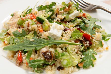 Angled shot of a couscous salad on a white plate. The salad ingredients consist of rocket, feta cheese, pinenuts and roasted peppers. nの写真素材