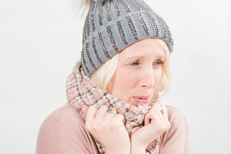 Blonde lady wearing a scarf and a winter beanie chilling over a white background
