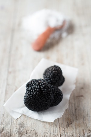 Pair of whole black truffles on a paper napkin with heap of salt and wooden spoon in the background on a wooden surfaceの写真素材
