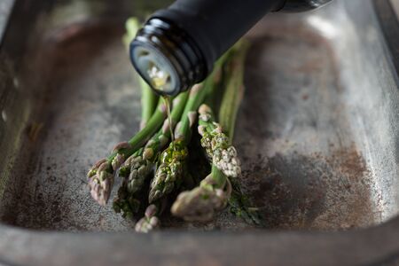 Closeup of olive oil being poured on a bunch of asparagus in baking trayの写真素材