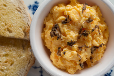 Overhead closeup of a bowl of scrambled eggs with grated truffles beside a pair of toasted bread