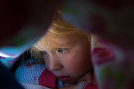 Closeup shot of a little girl looking over a glowing screen of a mobile deviceの写真素材