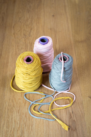 Spools of pink, yellow, and gray yarn on a wooden surface.