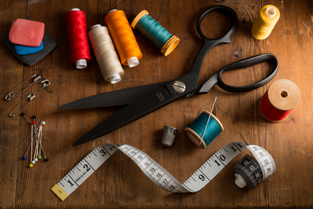 Spools of different color thread and basic sewing tools on a dimly lit wooden table topの写真素材