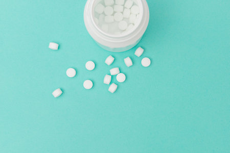 Overhead shot of scattered white pills and an opened medicine bottle with copy space