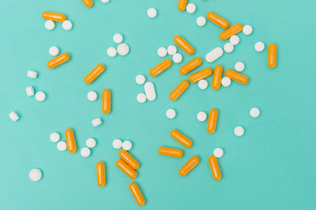 White round pills and orange-colored capsules scattered on a turquoise background