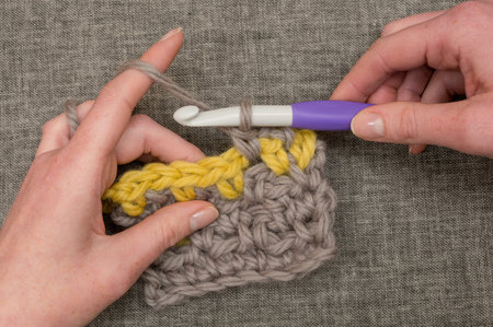 Hands knitting thick wool using a large crochet needle
