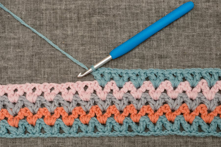Knitting hook making a loop in a crocheted band with colorful wavy pattern