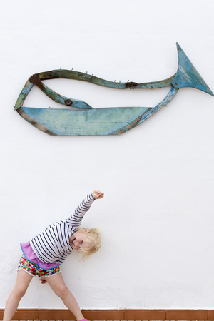 Little girl cheerfully posing under a wooden whale iconの写真素材