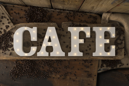 Decorative letters with illuminated embedded LED lights spelling the word CAFE surrounded with coffee beans over rustic wooden backgroundの写真素材